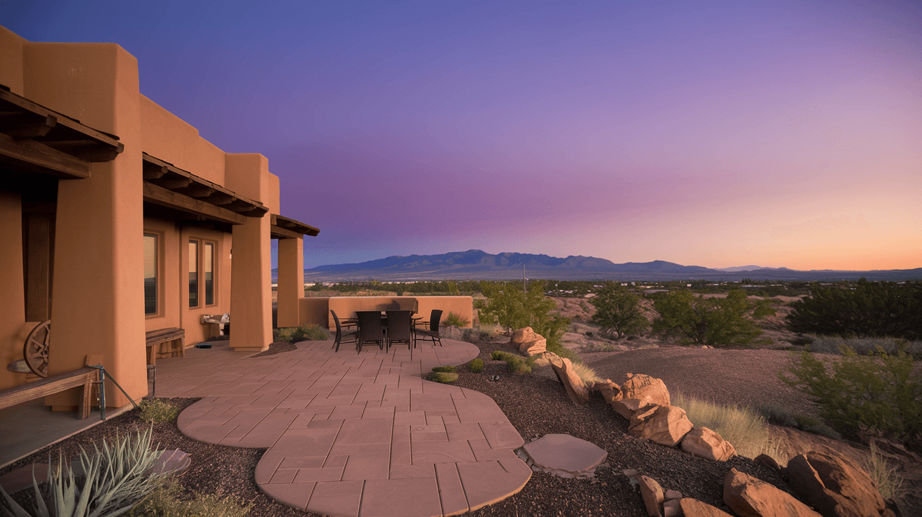 A modern Southwest-style home in Albuquerque's High Desert neighborhood with a flagstone patio overlooking open desert terrain, the Sandia Mountains filling the entire eastern horizon at dusk