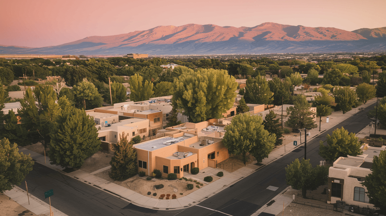 Aerial view of an Albuquerque residential neighborhood at golden hour, with the Sandia Mountains glowing pink in the background and tree-lined streets below