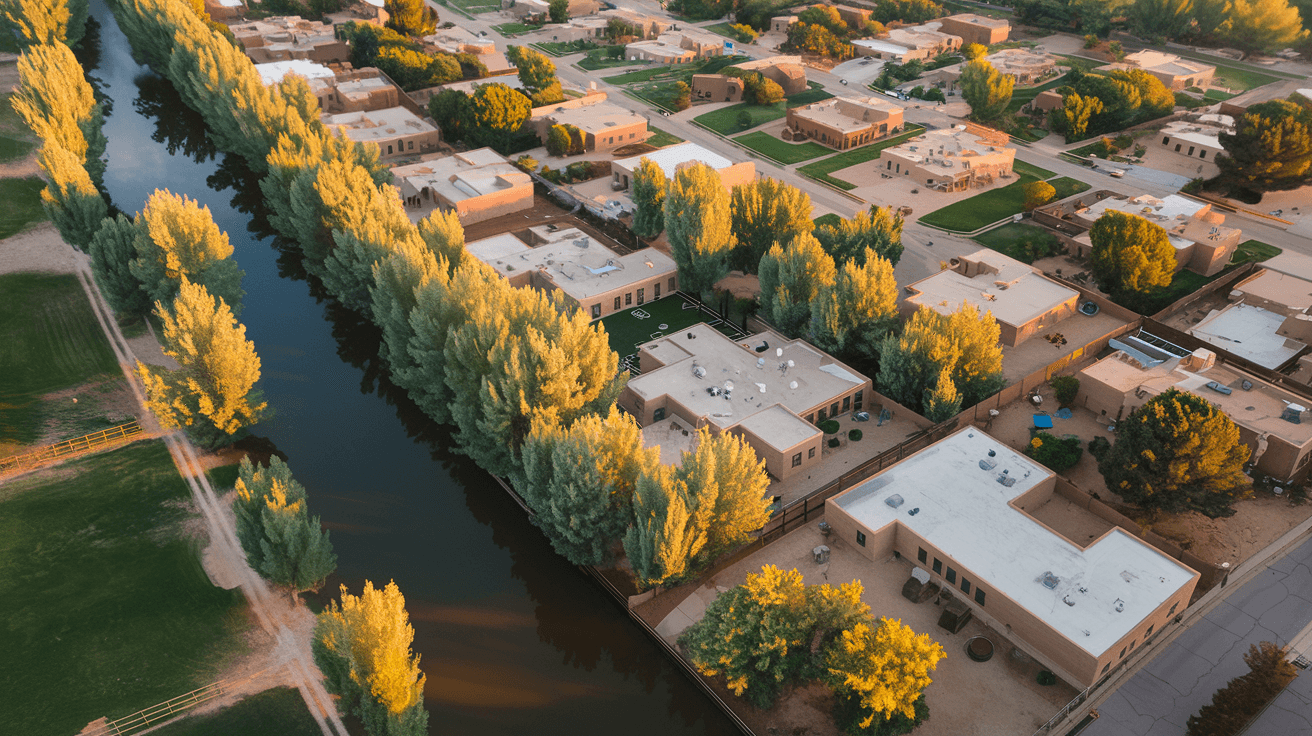 Aerial view of the North Valley neighborhood with cottonwood trees lining an acequia, horse pastures, and adobe homes stretching toward the Rio Grande bosque at golden hour
